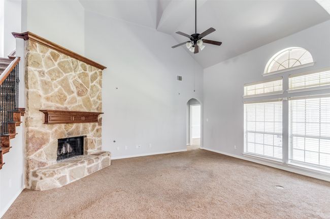 Unfurnished living room with high vaulted ceiling, carpet, a ceiling fan, a stone fireplace, and arched walkways | Image 9