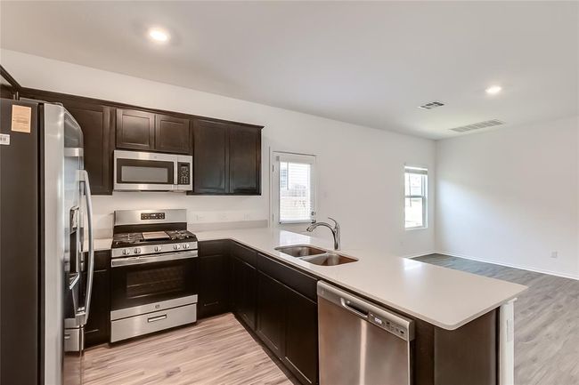 Kitchen with appliances with stainless steel finishes, a sink, light countertops, a peninsula, and dark brown cabinetry | Image 12