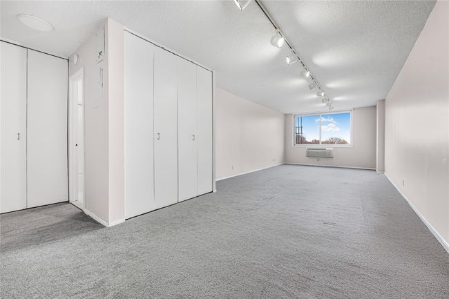 Unfurnished bedroom with multiple closets, carpet, a wall unit AC, rail lighting, and a textured ceiling | Image 4