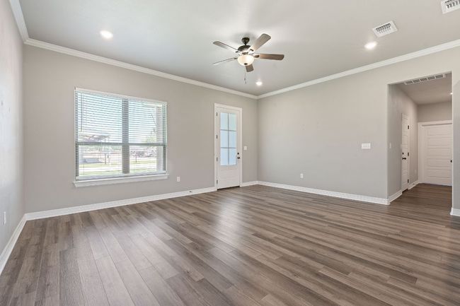 Empty room with a ceiling fan, dark wood finished floors, ornamental molding, and recessed lighting | Image 6
