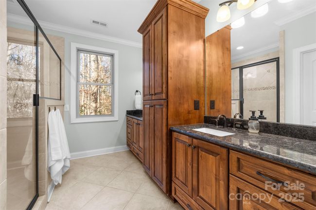 Primary bath has a large walk-in tile shower and beautiful cabinetry with dual sinks. | Image 19
