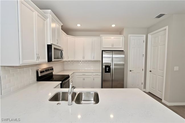 Kitchen with appliances with stainless steel finishes, a sink, white cabinetry, decorative backsplash, and recessed lighting | Image 14