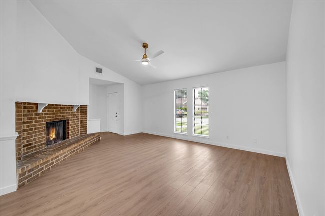 Unfurnished living room featuring wood finished floors, vaulted ceiling, baseboards, ceiling fan, and a fireplace | Image 9