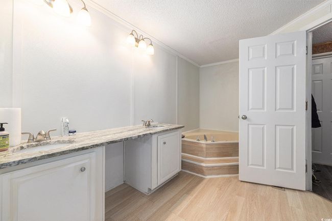 Bathroom with wood finished floors, a garden tub, a textured ceiling, double vanity, and ornamental molding | Image 18