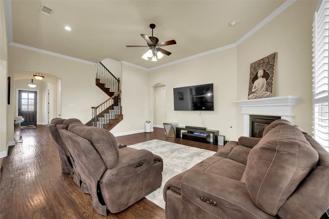 Living room featuring arched walkways, ornamental molding, dark wood finished floors, a glass covered fireplace, and stairway | Image 13