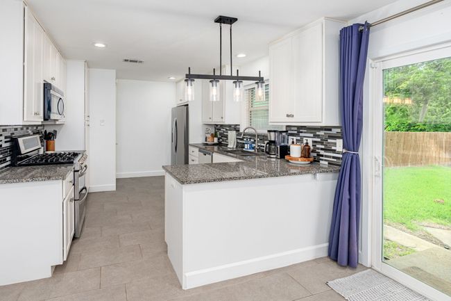 The kitchen has neutral tone granite with complimenting backsplash, shaker door cabinets, stainless appliances & updated fixtures. | Image 13