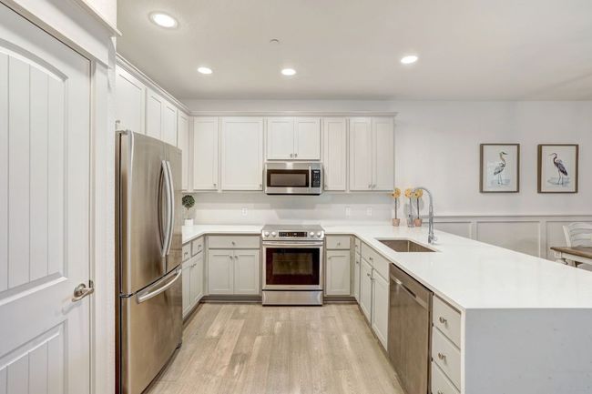 Kitchen with appliances with stainless steel finishes, a sink, a peninsula, light wood-type flooring, and light countertops | Image 8