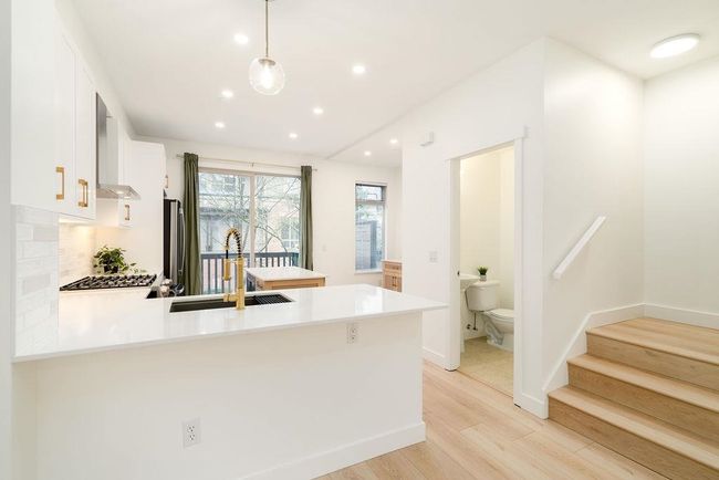 Kitchen with light countertops, a sink, light wood-style floors, wall chimney range hood, and a peninsula | Image 10