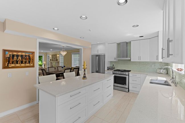 Kitchen featuring stainless steel appliances, wall chimney range hood, a center island, tasteful backsplash, and light stone countertops | Image 10