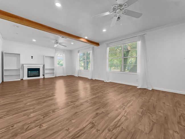 Unfurnished living room featuring ceiling fan, beamed ceiling, wood finished floors, recessed lighting, and a glass covered fireplace | Image 6