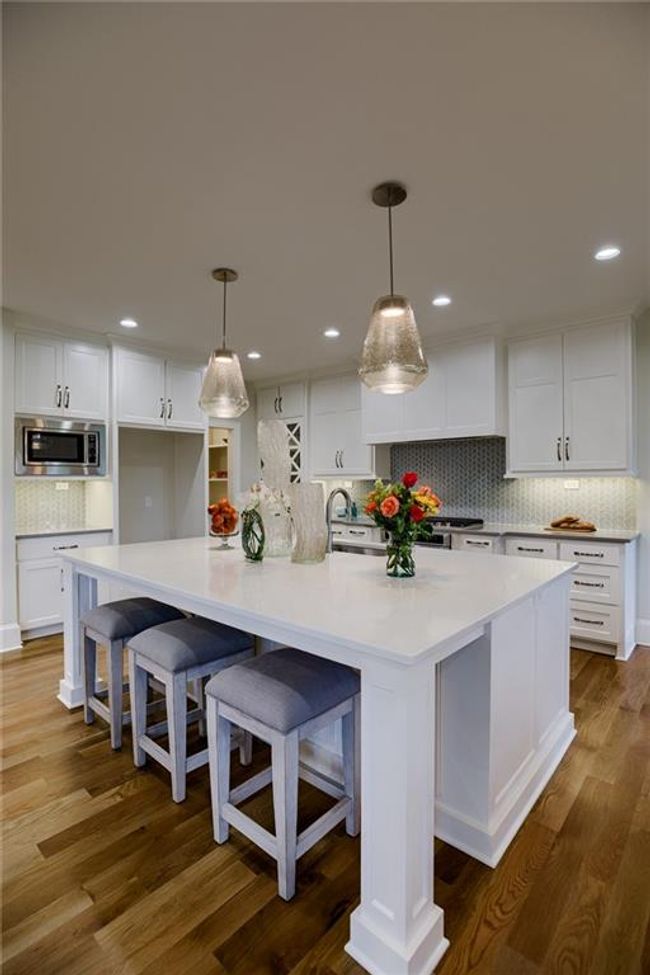 Kitchen with white cabinets, hardwood / wood-style flooring, stainless steel microwave, and a large island | Image 16