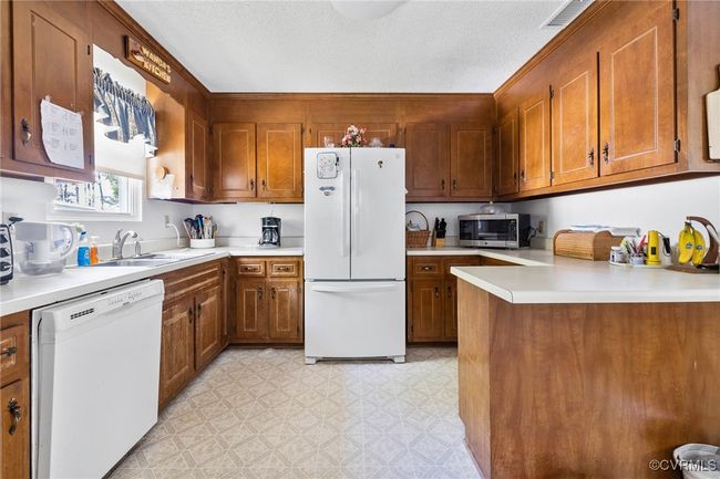 Kitchen with brown cabinets, a sink, white appliances, and light countertops | Image 23