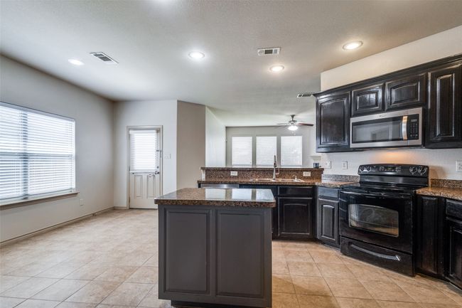 Kitchen with stainless steel microwave, electric range, a ceiling fan, a kitchen island, and a peninsula | Image 10