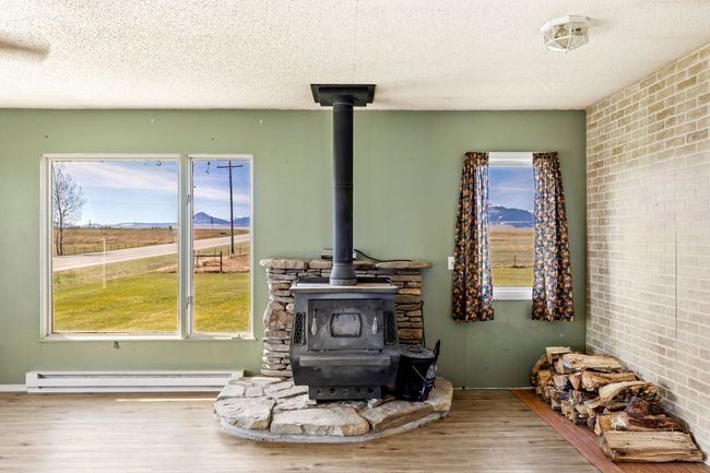 Interior details featuring a wood stove, wood finished floors, a textured ceiling, and a baseboard radiator | Image 15
