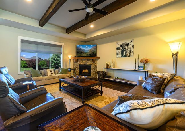 Living area with beam ceiling, wood finished floors, ceiling fan, a stone fireplace, and recessed lighting | Image 8