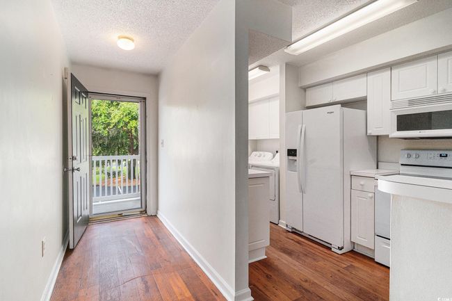 Kitchen with white appliances, a textured ceiling, white cabinetry, washing machine and clothes dryer, and hardwood / wood-style floors | Image 23