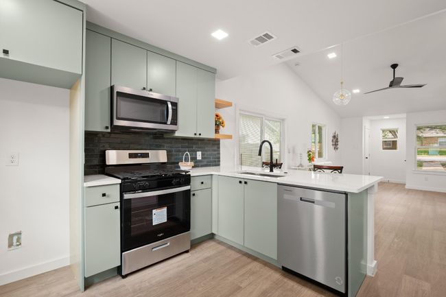Kitchen with stainless steel appliances, a peninsula, light wood-style flooring, light countertops, and lofted ceiling | Image 13