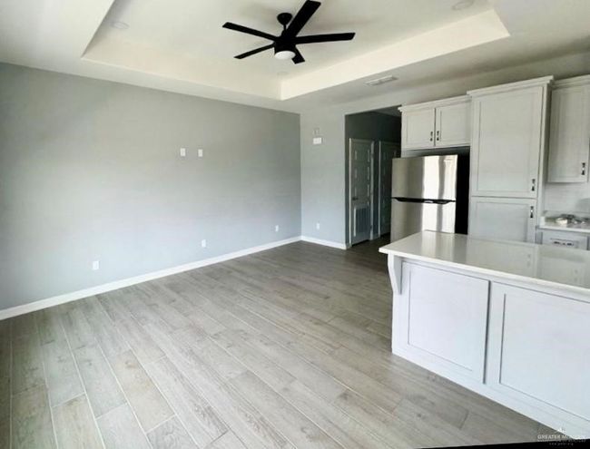 Kitchen with baseboards, a raised ceiling, freestanding refrigerator, light countertops, and white cabinetry | Image 6