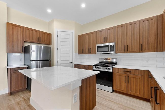 Kitchen with stainless steel appliances, light wood-style flooring, a kitchen island, decorative backsplash, and brown cabinets | Image 13