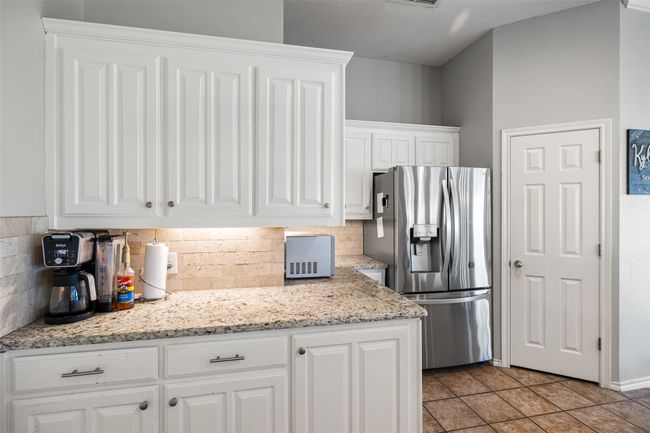 Kitchen featuring white cabinets, light tile patterned flooring, tasteful backsplash, stainless steel fridge with ice dispenser, and light stone countertops | Image 12
