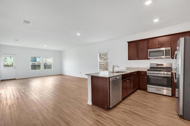Kitchen with visible vents, a peninsula, stainless steel appliances, a sink, and open floor plan | Image 6
