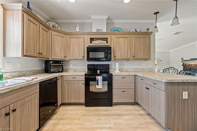 Kitchen featuring light grey cabinets, light countertops, black appliances, light wood finished floors, and a peninsula | Image 9