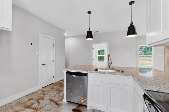 Kitchen with stainless steel appliances, white cabinets, light stone counters, and hanging light fixtures | Image 20