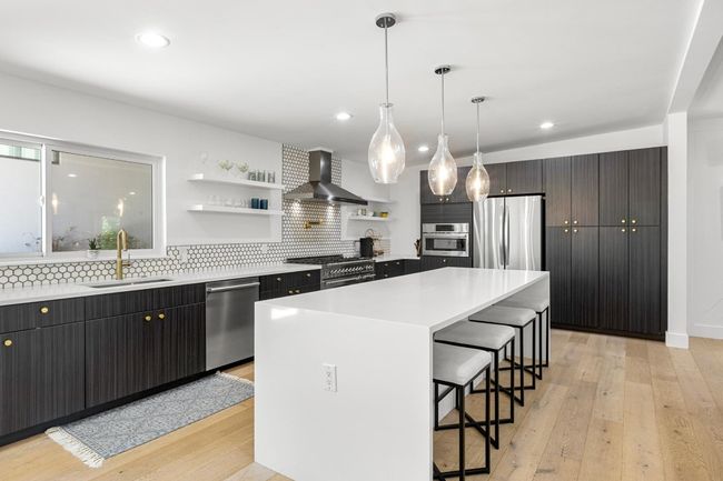 Kitchen with open shelves, a sink, wall chimney range hood, appliances with stainless steel finishes, and a breakfast bar area | Image 9