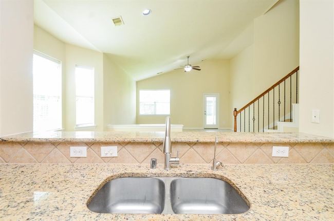 Bright and open living area with high ceilings, visible from the kitchen featuring granite countertops and a double sink. Stairs with decorative railing lead to the upper level, and large windows provide ample natural light. | Image 13