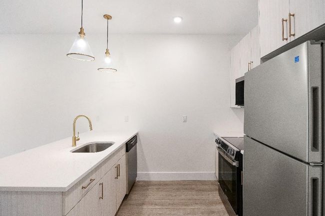 Kitchen featuring stainless steel appliances, a sink, a peninsula, light countertops, and light wood finished floors | Image 34