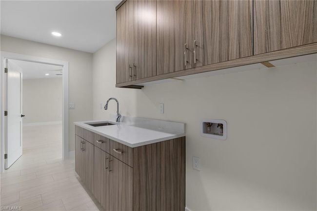 Clothes washing area featuring hookup for a washing machine, light tile patterned floors, cabinets, and sink | Image 46
