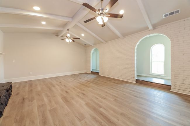 Unfurnished living room featuring arched walkways, brick wall, a ceiling fan, light wood-style floors, and recessed lighting | Image 7