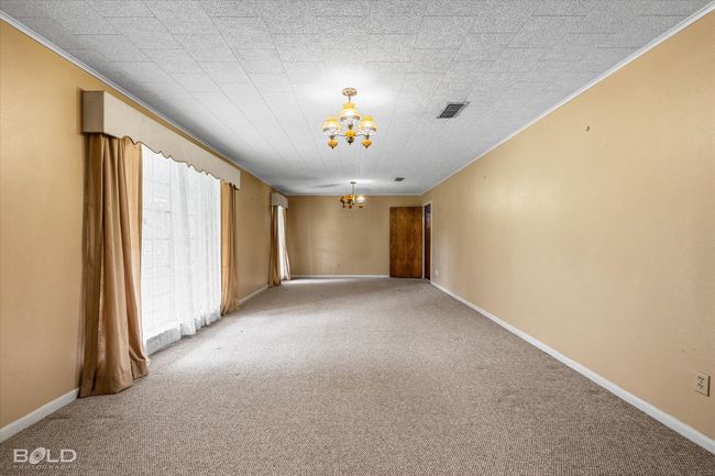 Living room with a chandelier, ornamental molding, light colored carpet, and baseboards | Image 6