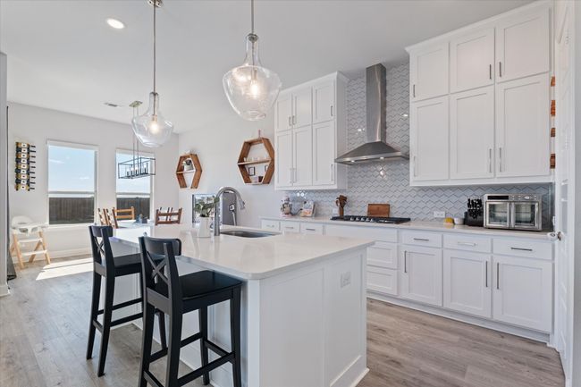 Kitchen featuring wall chimney exhaust hood, a sink, light countertops, decorative backsplash, and light wood finished floors | Image 7