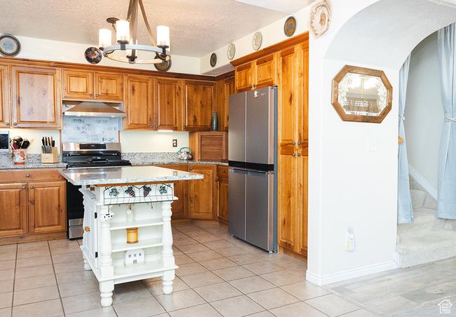 Kitchen with appliances with stainless steel finishes, open shelves, under cabinet range hood, a chandelier, and brown cabinetry | Image 4