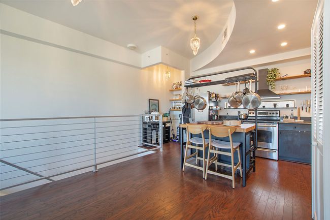 Kitchen featuring stainless steel range with electric stovetop, open shelves, a kitchen breakfast bar, wall chimney exhaust hood, and dark wood finished floors | Image 10