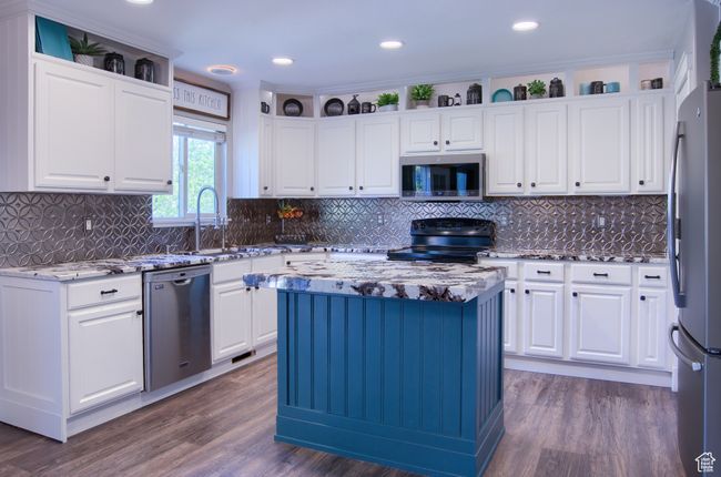 Kitchen featuring stainless steel appliances, white cabinetry, dark wood-type flooring, and light stone counters | Image 5