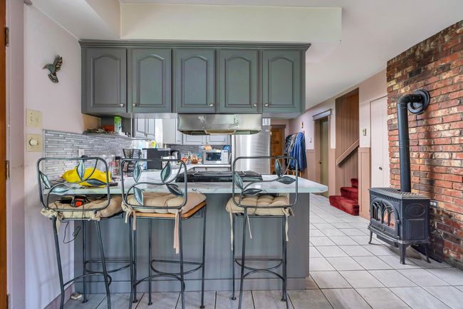 Kitchen with a kitchen breakfast bar, tasteful backsplash, a peninsula, light tile patterned floors, and a wood stove | Image 6