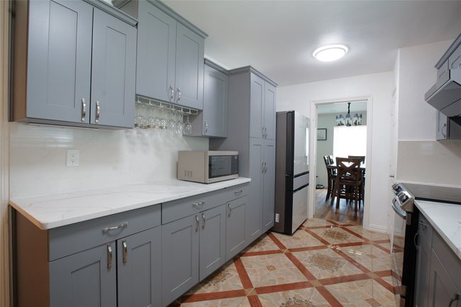 Kitchen featuring appliances with stainless steel finishes, gray cabinets, light stone countertops, and a chandelier | Image 13