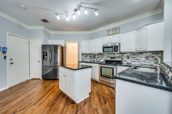 Kitchen featuring appliances with stainless steel finishes, backsplash, dark wood-style flooring, a kitchen island, and white cabinetry | Image 6