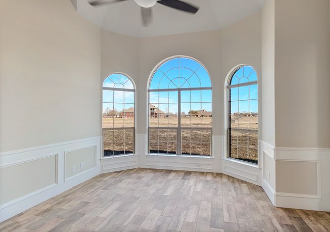 Spare room featuring a ceiling fan, wood finished floors, wainscoting, a high ceiling, and a decorative wall | Image 10