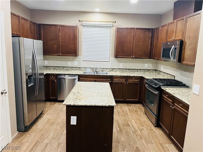 Kitchen featuring a kitchen island, decorative backsplash, appliances with stainless steel finishes, light wood-style floors, and a sink | Image 5