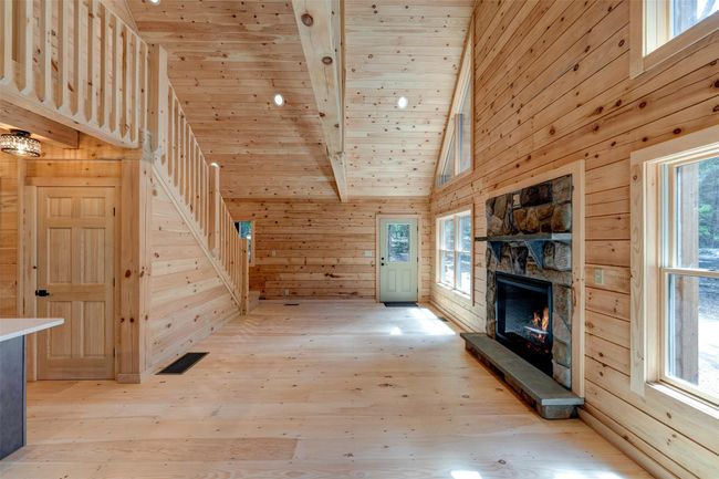 Unfurnished living room featuring wood walls, light wood-type flooring, high vaulted ceiling, wood ceiling with exposed beams, and a fireplace | Image 11