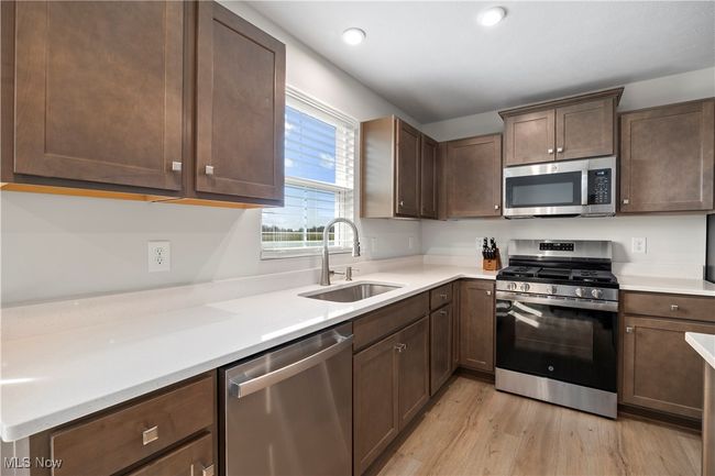 Kitchen featuring light wood-type flooring, dark brown cabinets, light countertops, a sink, and stainless steel appliances | Image 18