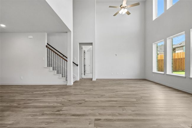 Unfurnished living room with a high ceiling, stairs, ceiling fan, and light wood-style floors | Image 14