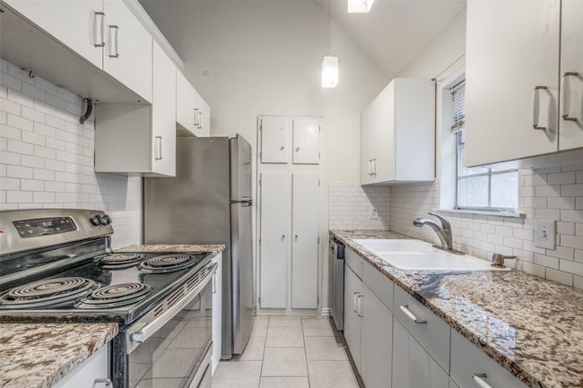 Kitchen with stainless steel appliances, lofted ceiling, light tile patterned floors, white cabinets, and backsplash | Image 12