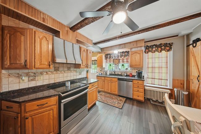 Kitchen with stainless steel appliances, ventilation hood, a sink, radiator heating unit, and dark wood-style floors | Image 10