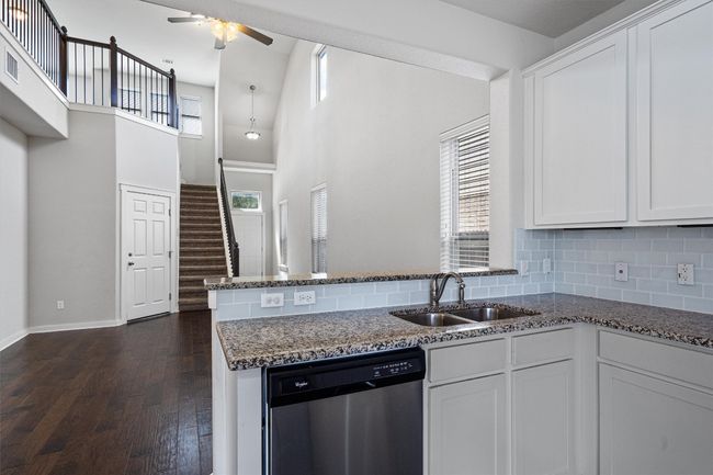 Kitchen with dishwasher, ceiling fan, dark stone counters, white cabinets, and a towering ceiling | Image 19