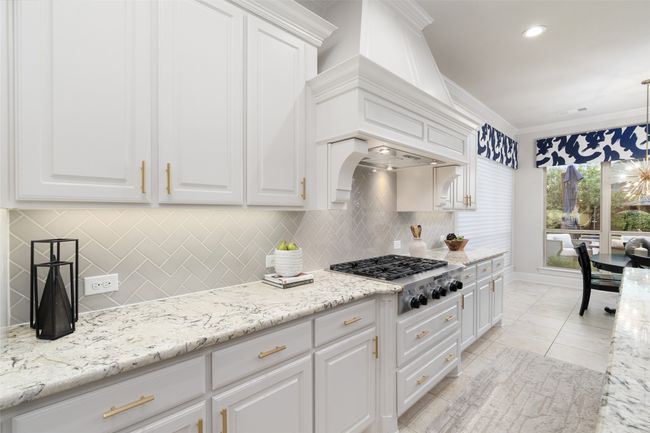 Gorgeous herringbone backsplash, professional vent hood, pot drawers, 6 burner gas cooktop and upgraded granite countertops look amazing with the white cabinetry. Bright and airy for any chef. | Image 14