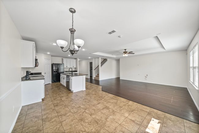 Kitchen featuring dark countertops, black refrigerator with ice dispenser, open floor plan, white cabinetry, and a center island with sink | Image 17
